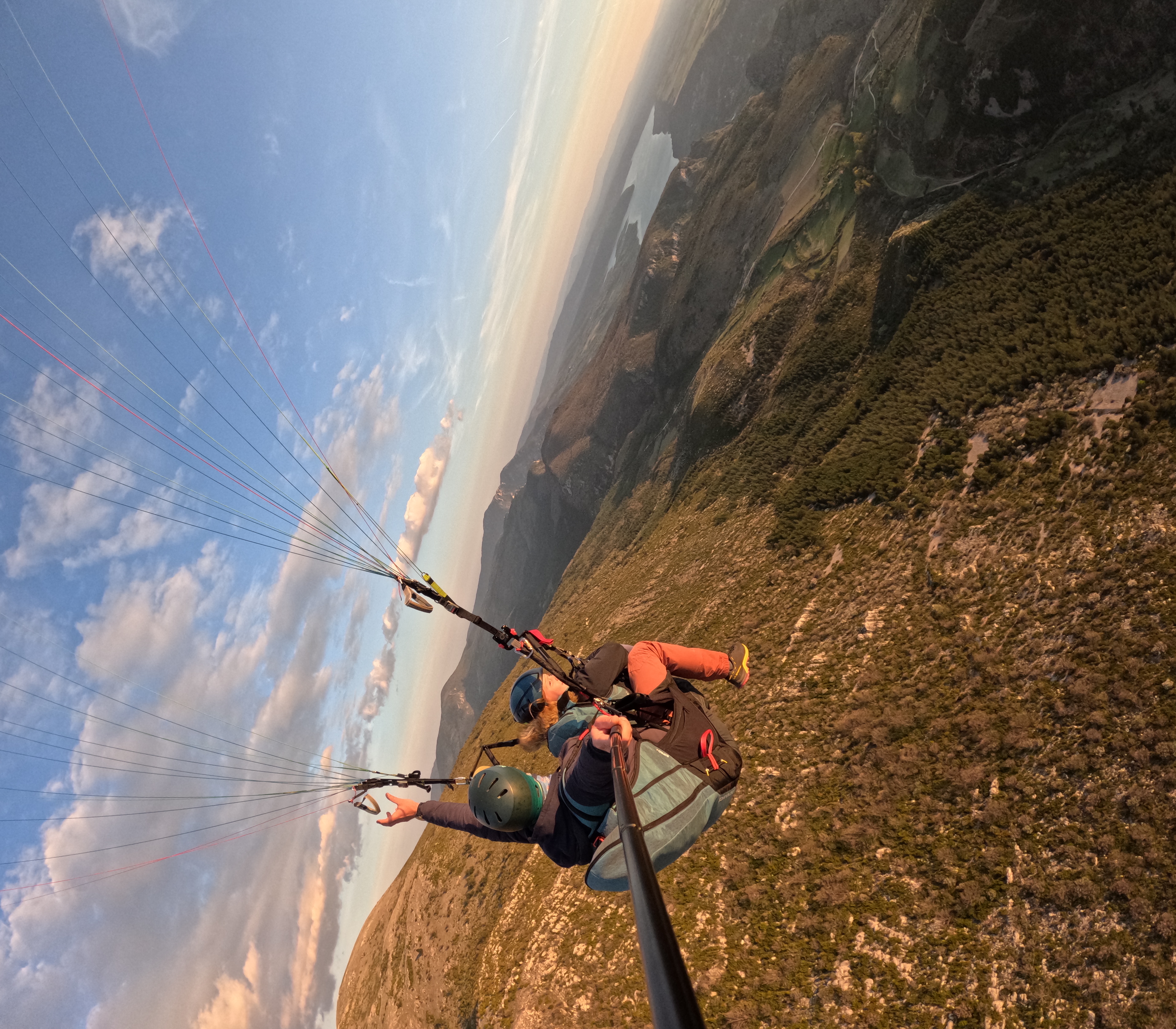 Passager souriant, bras tendu, pendant un vol en parapente biplace en Haute-Savoie