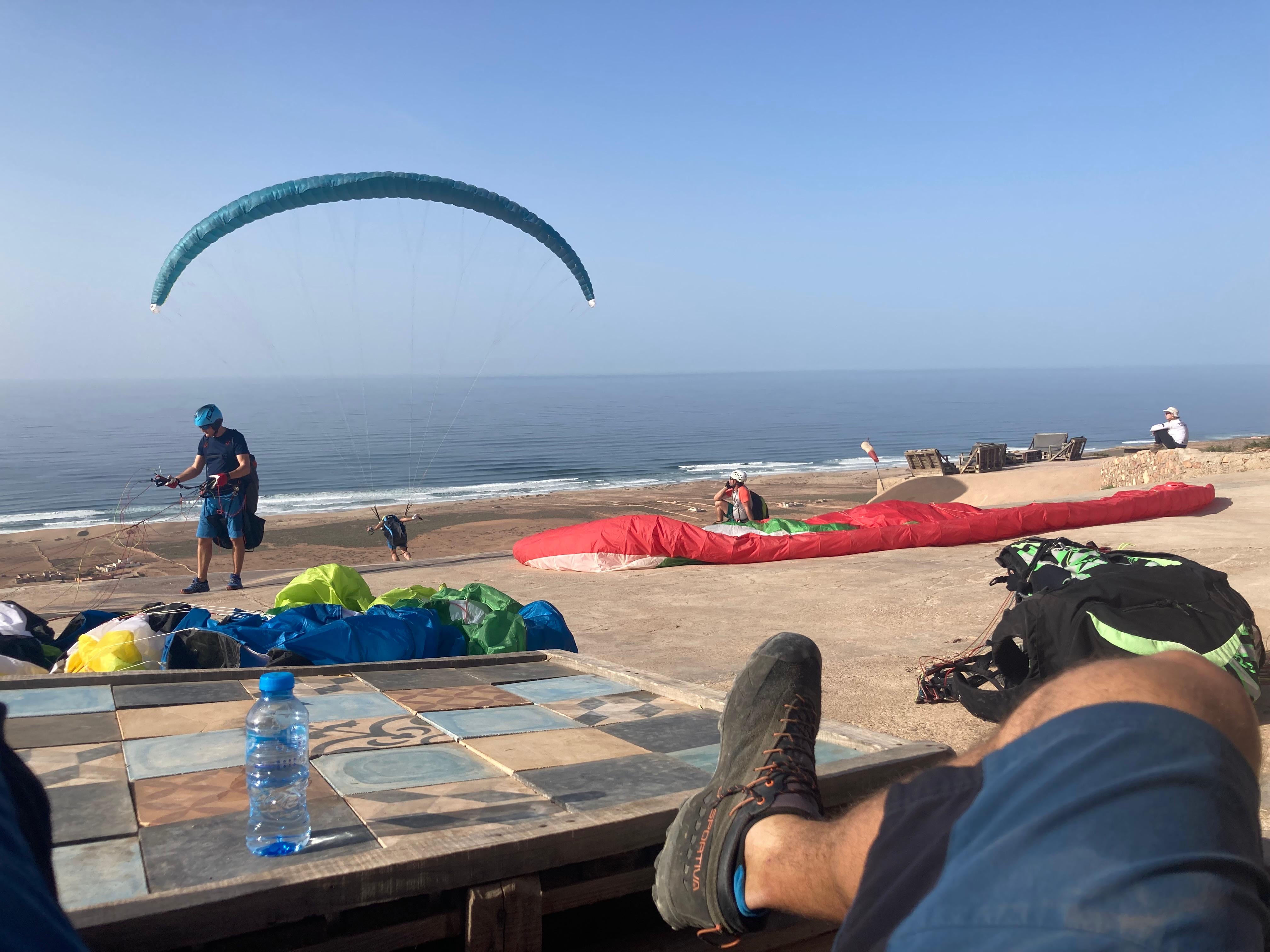 Pilotes en pause sur la terrasse du site de vol, observant les conditions face à l’océan